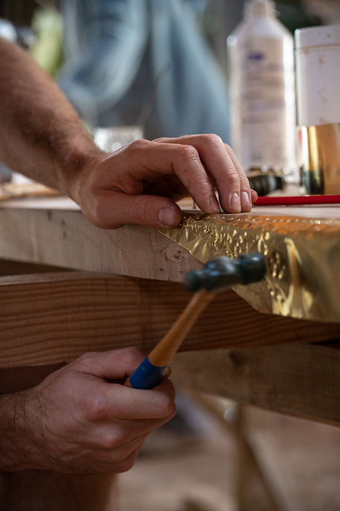 Gros plan des mains de Kilian avec un marteau sur la tranche de la table
